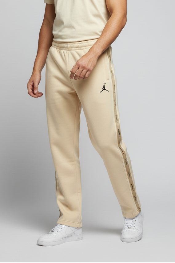 Man wearing a beige t-shirt and pants with a logo, standing against a plain background