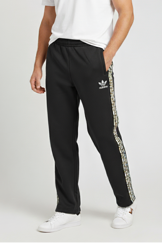 Man wearing a white t-shirt and black Adidas tracksuit with a snake print stripe on a white background