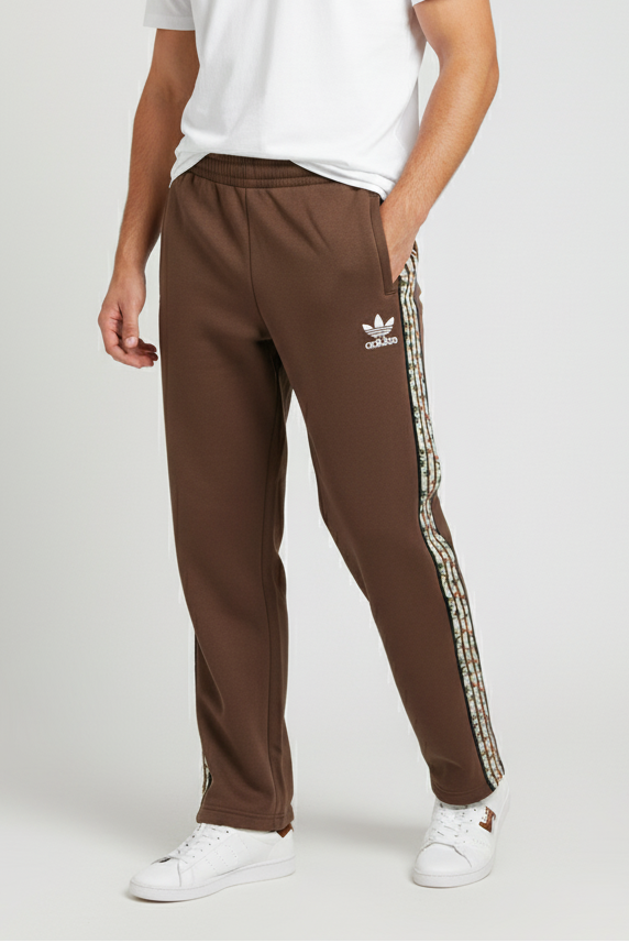 Man wearing a white t-shirt and brown Adidas tracksuit pants on a light gray background